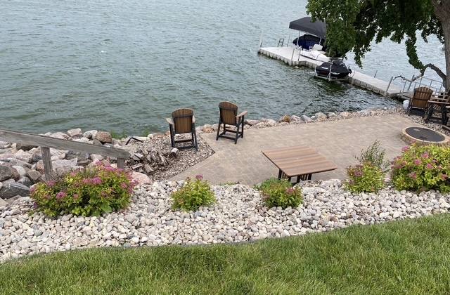 Lakeside paver patio with seating and decorative rock beside the water