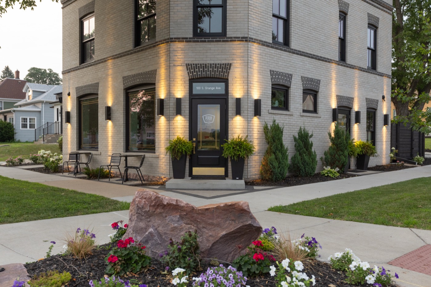 Uplit brick building corner with a boulder and flower beds at The Perch