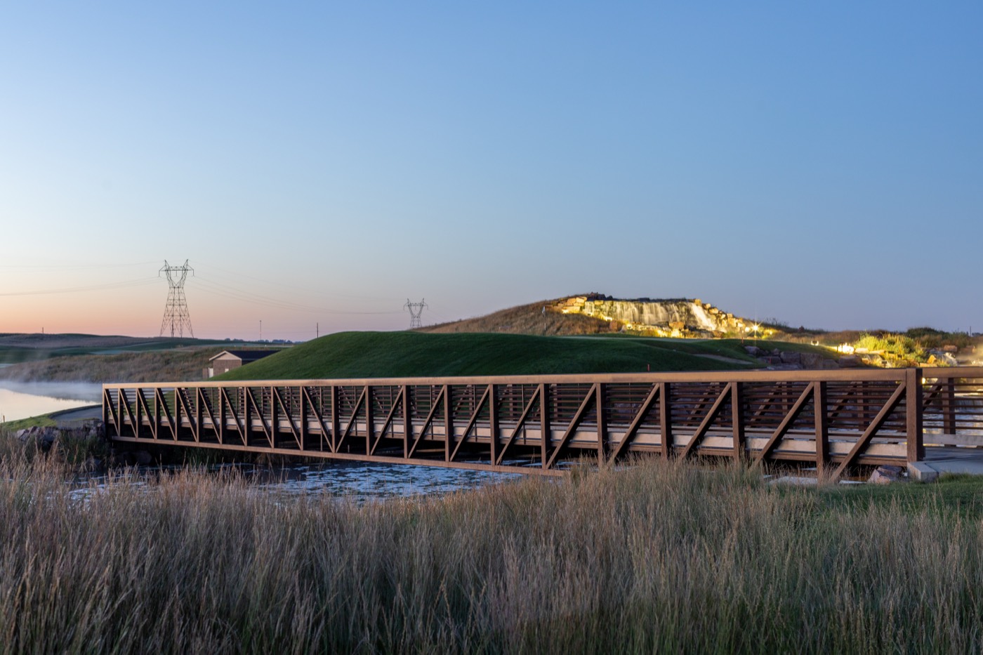 Timber footbridge over water with a landscaped hillside, Grand Falls Casino & Resort